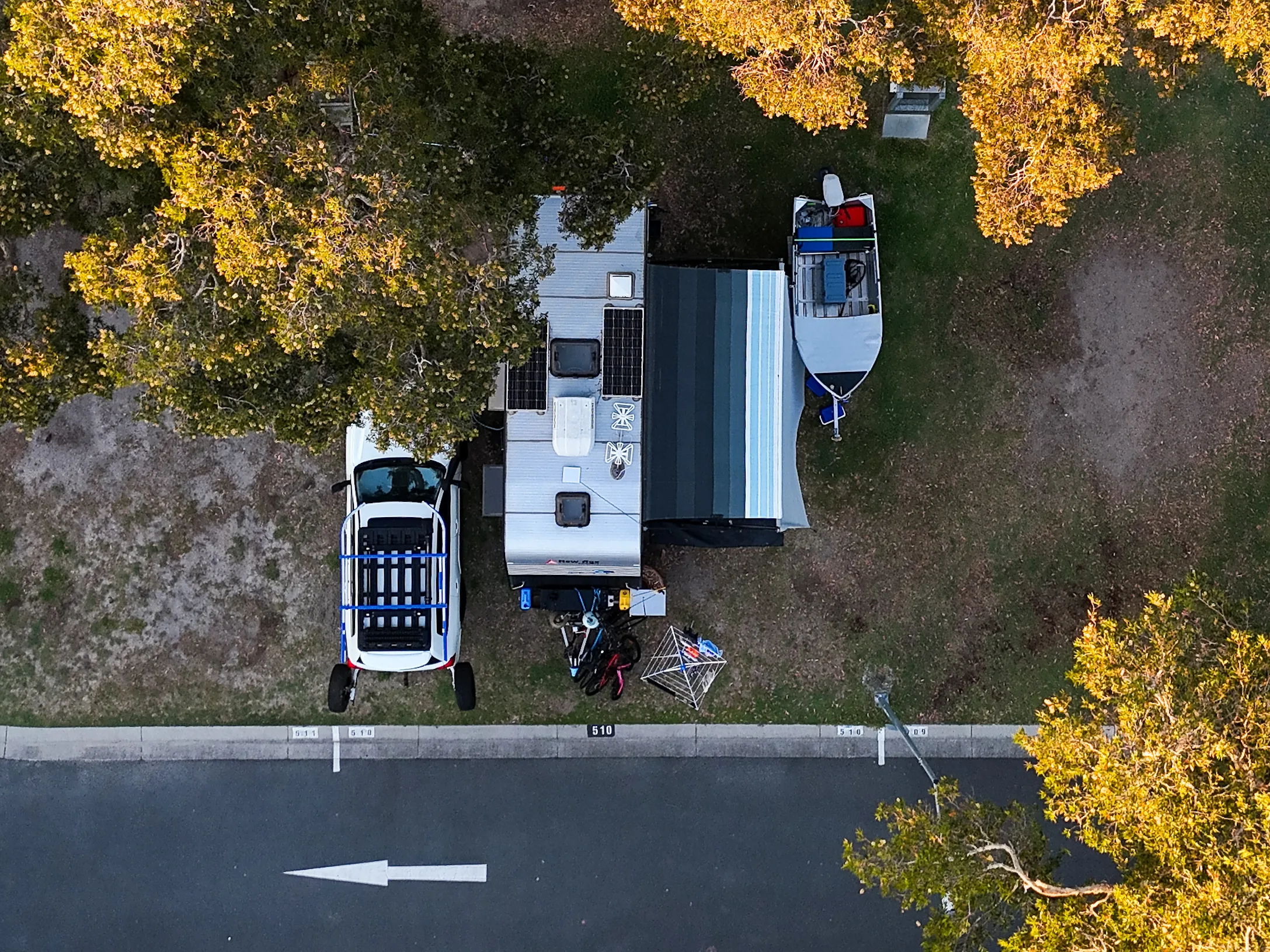 Roam N Round’s caravan, 4WD and boat set up at a shaded campsite, seen from above