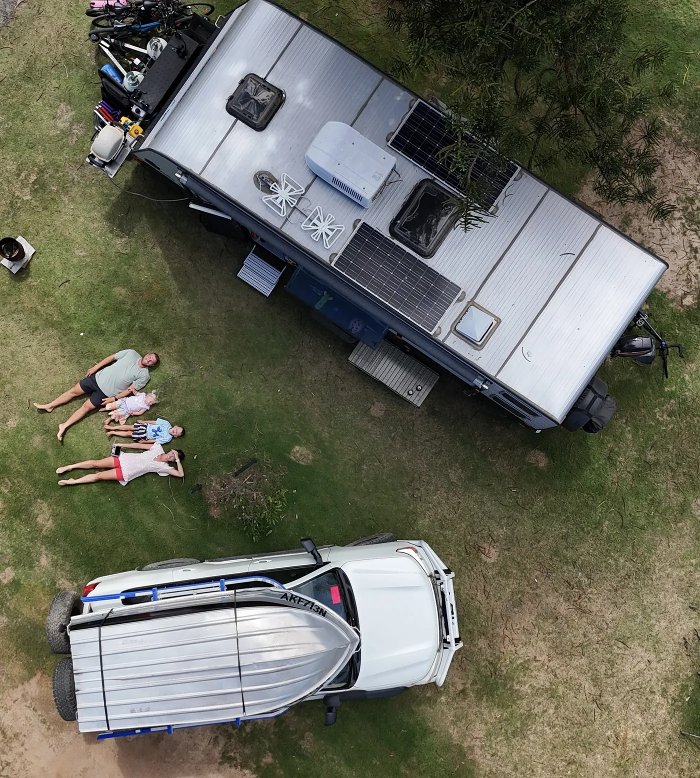 Brittany, Shaun, Max and Allie lying on the grass beside their caravan and 4WD, seen from above