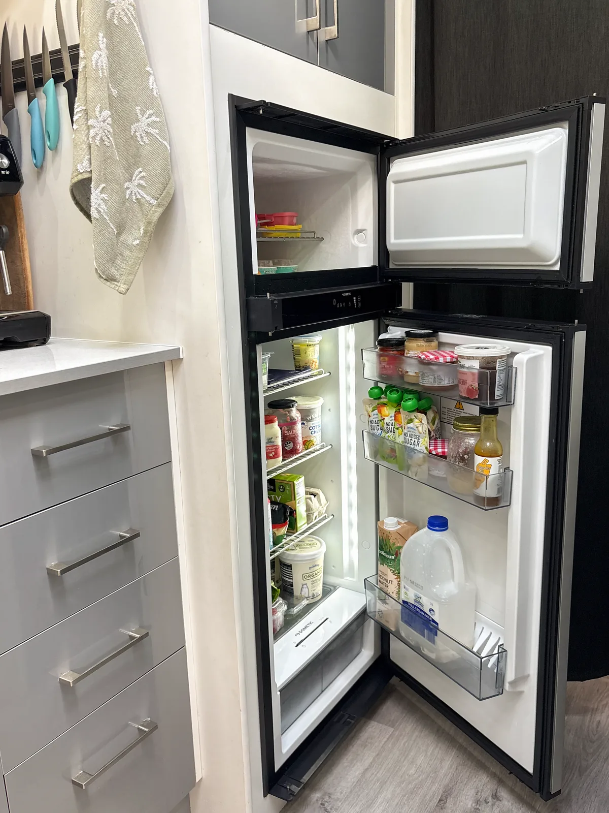 The Dometic fridge and freezer open and stocked with drinks, sauces and groceries
